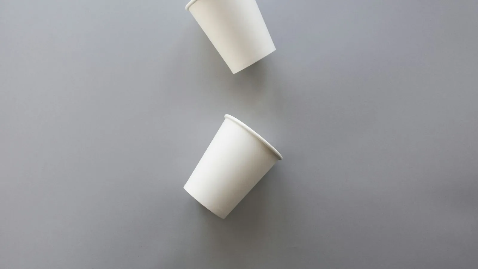 Two white disposable cups on gray surface